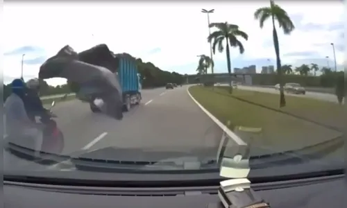 Vídeo: Lona se solta de caminhão e causa acidente de moto