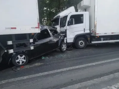 Um carro de passeio foi prensado por dois caminhões