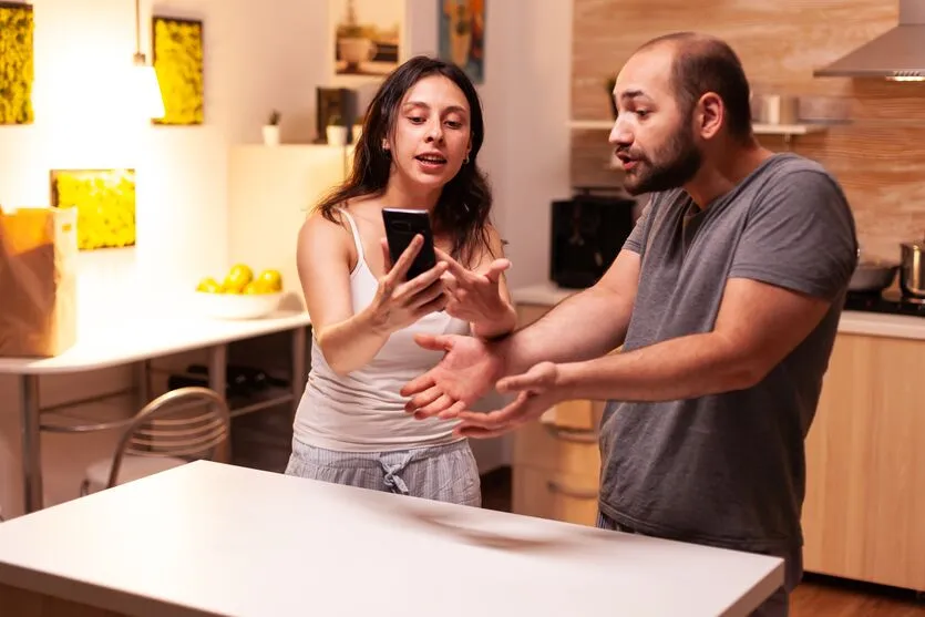 Woman pointing at phone while reading messages of infidel husband while having a disagreement. Heated angry frustrated offended irritated accusing her man of cheating.