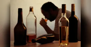  silhouette of anonymous alcoholic person drinking behind bottles of alcohol 