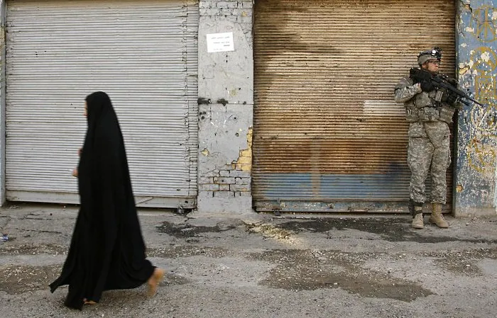  Mulher caminha em rua de Bagdá vigiada por militar americano; documentos secretos vazados pelo site WikiLeaks revelaram a morte de 680 civis em bloqueios no Iraque