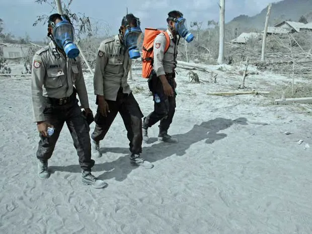  Policiais usam máscaras para investigar povoado atingido por nuvem de cinzas do vulcão Merapi em Kinahrejo, na Indonésia