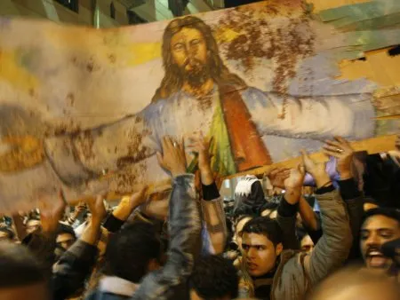  Cristãos coptas carregam imagem de Cristo manchada com sangue de vítimas de atentado em frente a igreja de Alexandria, no Egito, neste domingo (2)