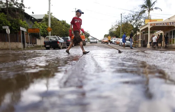  Menino usa vassoura para empurrar lama nas ruas de Brisbane, na Austrália; mortos em enchentes chegam a 15