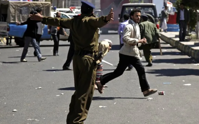  Policial tenta impedir que manifestantes pró-governo joguem pedras em opositores durante protestos em Sanaa, capital do Iêmen