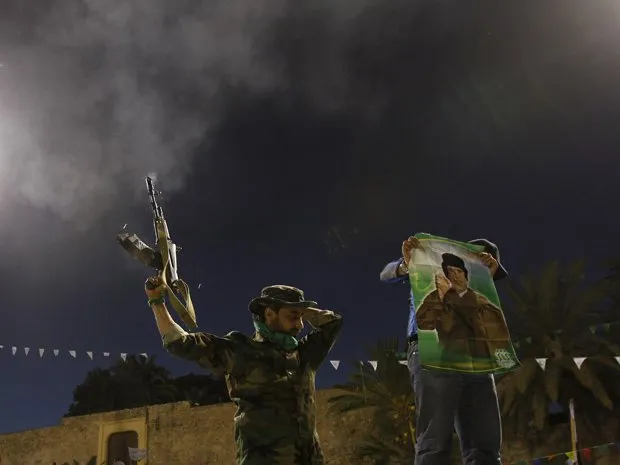  Soldado leal a Kadhafi dá tiros para o ar neste domingo (20) em Trípoli, capital da Líbia, enquanto colega mostra cartaz com a imagem do ditador