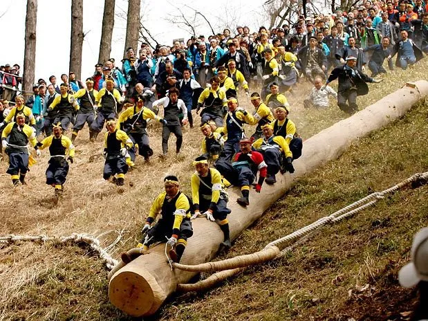   Homens descem ladeira montados em tronco de árvore durante o "Onbashira", no Japão