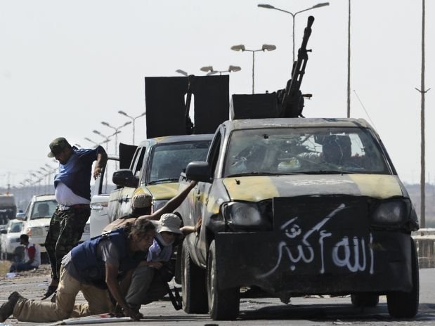 Combatentes se protegem atrás de caminhões blindados durante troca de tiros com forças de Kadafi nos arredores de Trípoli