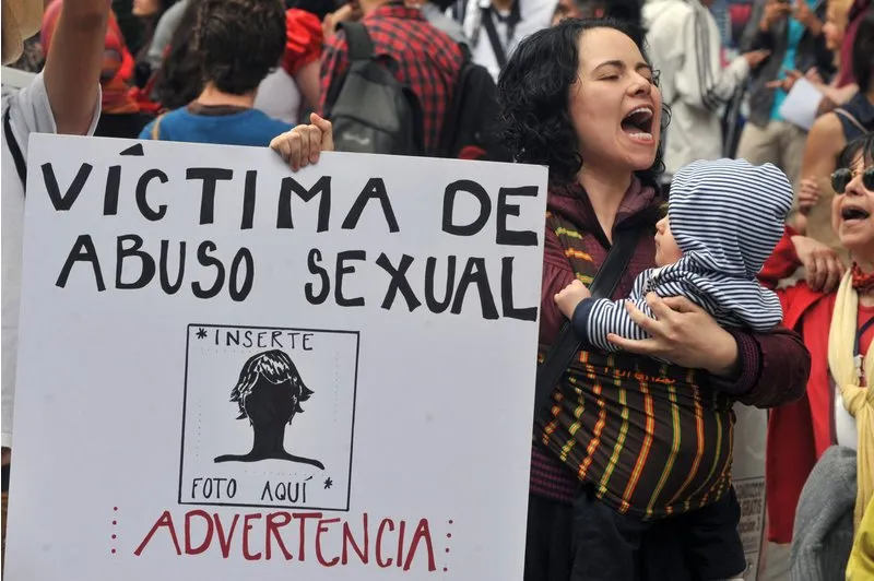 Mulher carrega um bebê e grita slogans enquanto segura cartaz com a frase "Vítima de abuso sexual" Foto: GUILLERMO LEGARIA / AFP / Getty