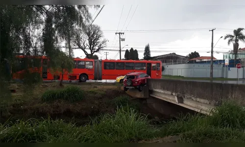 Carro bate contra ônibus e fica pendurado em ponte