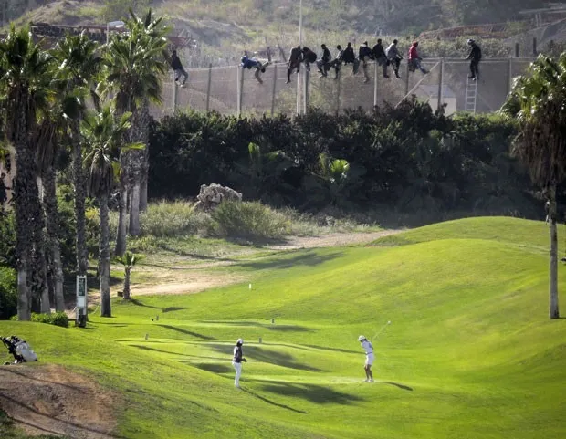Imigrantes ilegais tentam entrar no enclave espanhol de Melilla, no norte da África, em meio a um jogo de golfe que acontecia dentro do território nesta quarta-feira (22) (Foto: Jose Palazon/Reuters)
