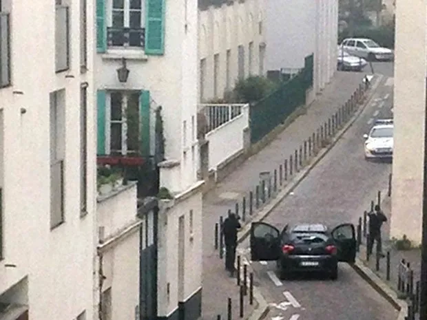 Homens armados são vistos saindo de um carro e apontando armas a um carro da polícia perto do escritório da revista satírica 'Charlie Hebdo', em Paris (Foto: Anne Gelbard/AFP)