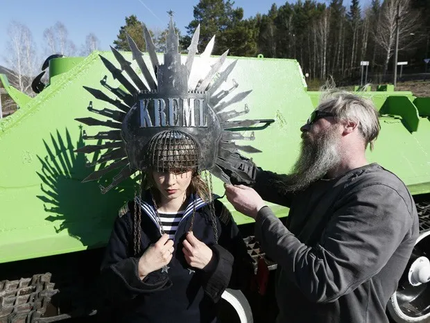 Modelo posa com chapéu de ferro bizarro em frente a monumento de guerra em Krasnoyarsk, na Rússia (Foto: Ilya Naymushin/Reuters)