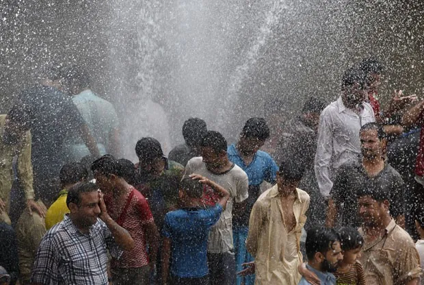 Pessoas se aliviam do forte calor com spray de água em Karachi, no Paquistão, nesta quinta-feira (25) (Foto: Akhtar Soomro/Reuters)