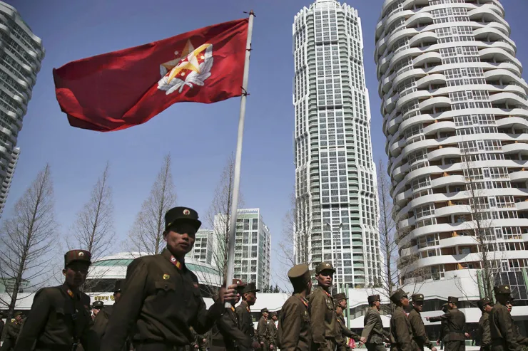   Soldados norte-coreanos carregam a bandeira do Exército do Povo enquanto passam por edifícios residenciais em Pyongyang, Coréia do Norte - Foto - AP-Yonhap - 13 de abril