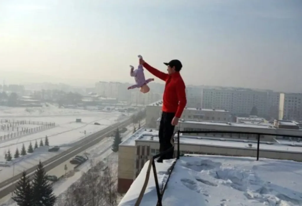 Russo posa na borda do telhado segurando filha bebê (ou boneca?) de cabeça para baixo - Foto: Siberian Times